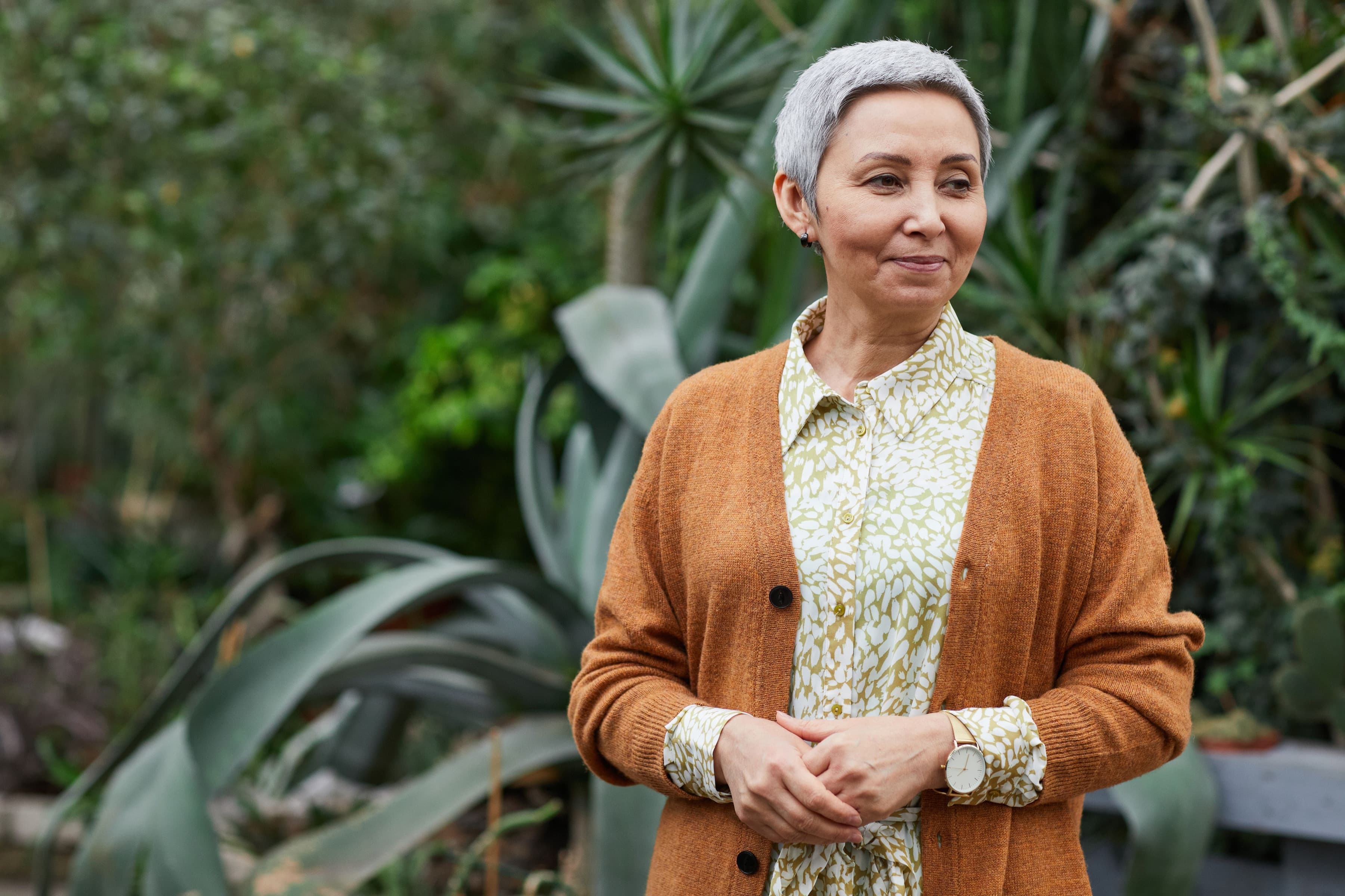 A woman with short silver hair smiling to herself in a garden