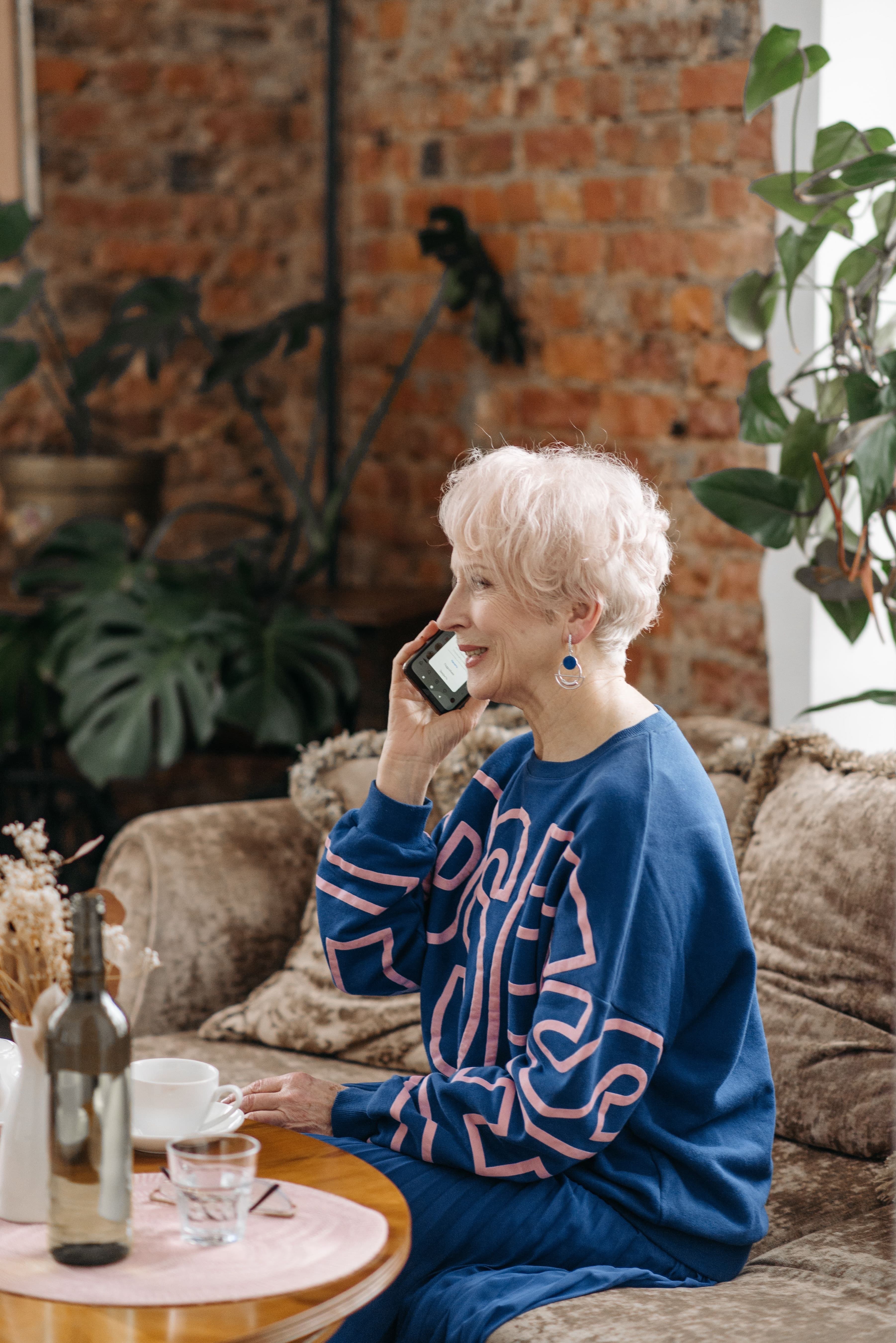 A woman with white hair smiling on a phone call on her sofa